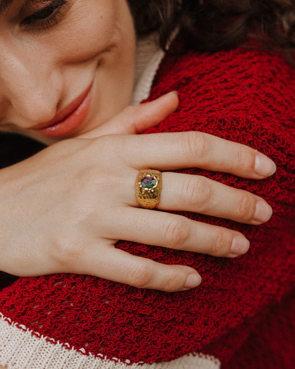 Primer plano de la modelo con cara alegre llevando en la mano el anillo bañado en oro de 18 quilates con piedra semipreciosa Rubí Zoisita de Isla Vurma