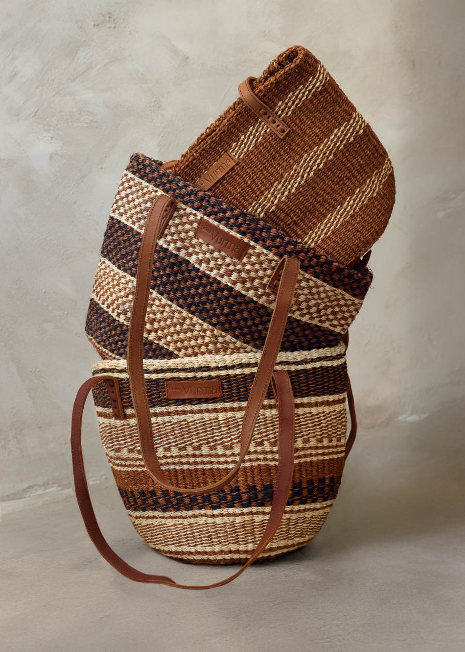 Bodegón de bolsos de sisal artesanales de Isla Vurma en tonos tierra y rayas étnicas, con asas de cuero - colección de bolsos sostenibles estilo boho para verano