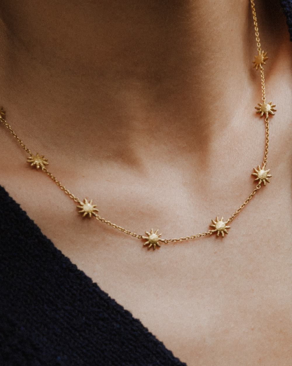 Primer plano de un collar dorado con pequeñas estrellas de ocho puntas alrededor del cuello de la modelo