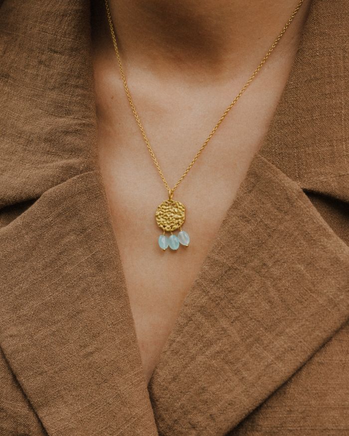 Primer plano del cuello de la modelo llevando el collar bañado en oro de 18 quilates con una pieza circular martillado con tres piedras semipreciosas en forma de gota en Aqua Calcedonia de Isla Vurma