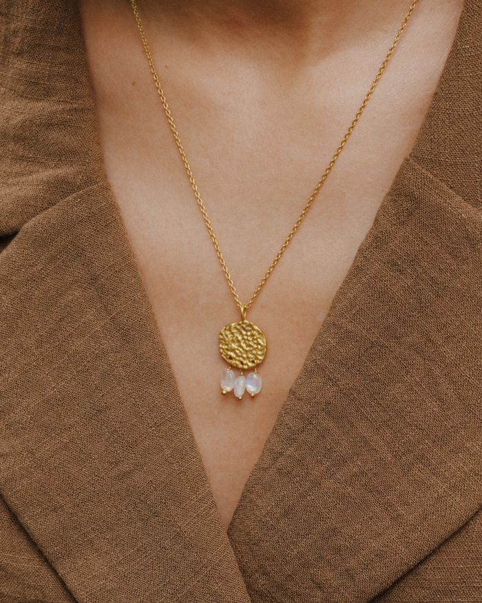 Primer plano del cuello de la modelo llevando el collar bañado en oro de 18 quilates con una pieza circular martillado con tres piedras semipreciosas en forma de gota en Piedra de Luna de Isla Vurma