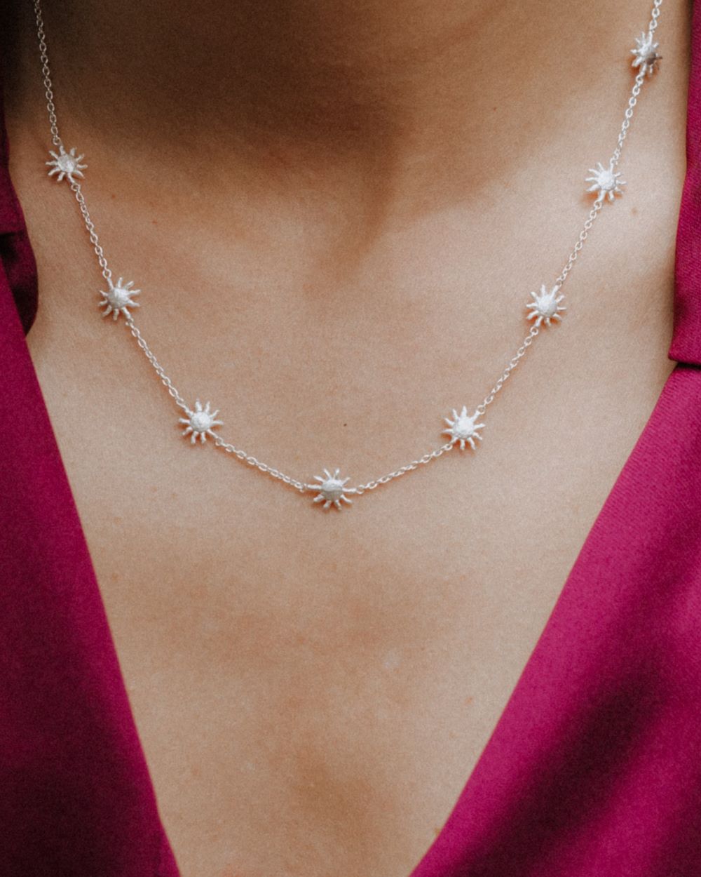 Primer plano de un collar plateado con pequeñas estrellas unidas por una fina cadena, colocado sobre el cuello de la modelo que lleva una blusa de color fucsia.