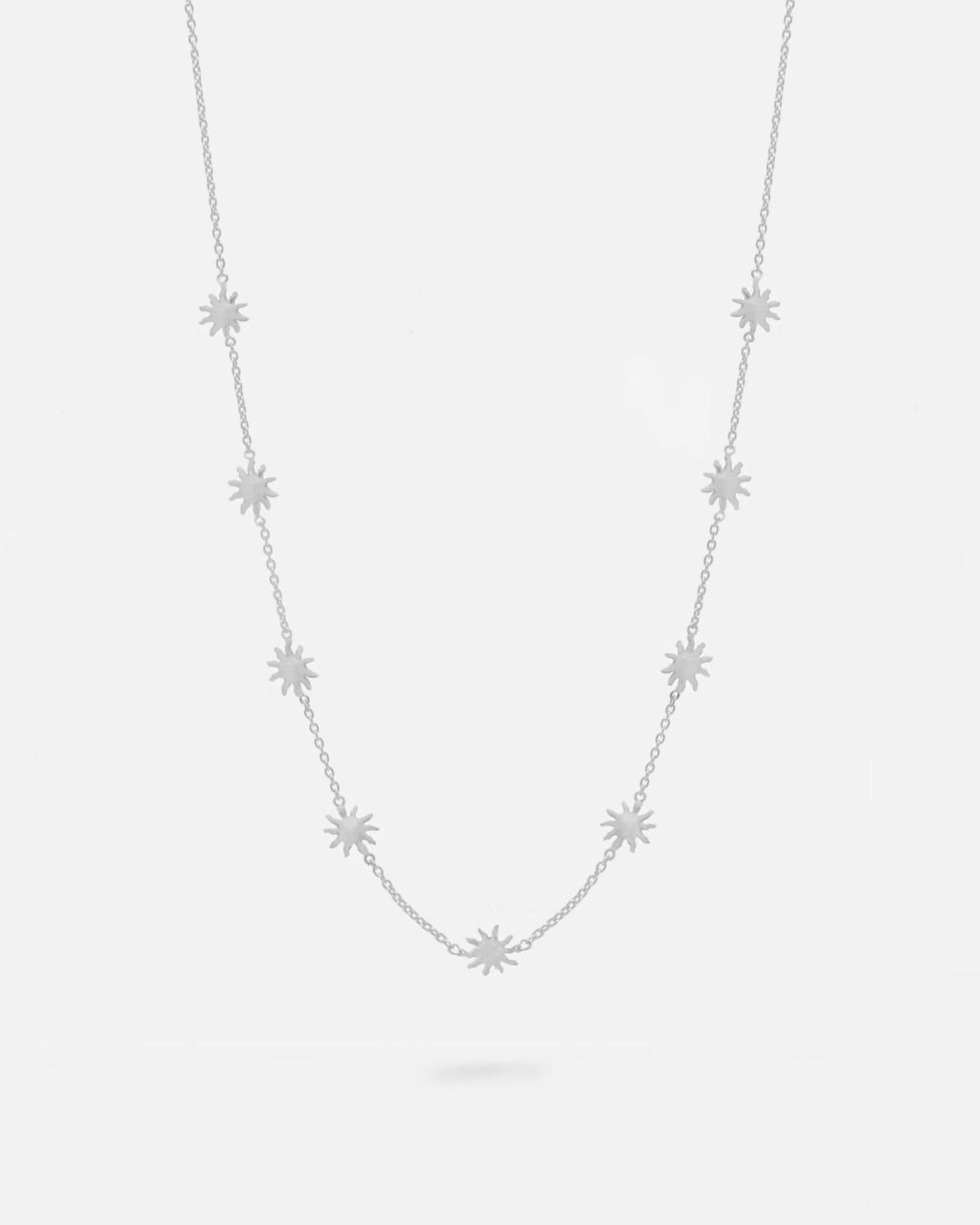 Collar plateado con pequeñas estrellas distribuidas de forma uniforme a lo largo de una cadena fina. Fondo liso y claro.
