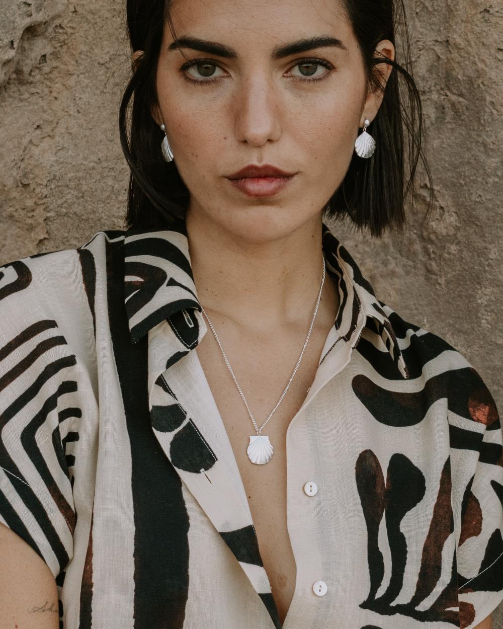 Modelo que lleva puesto un conjunto de collar y pendientes en forma de concha en tonalidad plateada