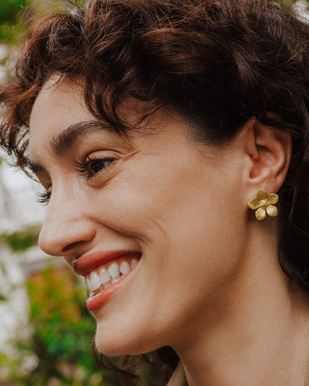 Pendiente dorado con forma de flor de cinco pétalos texturizados lucido en la oreja de la modelo.