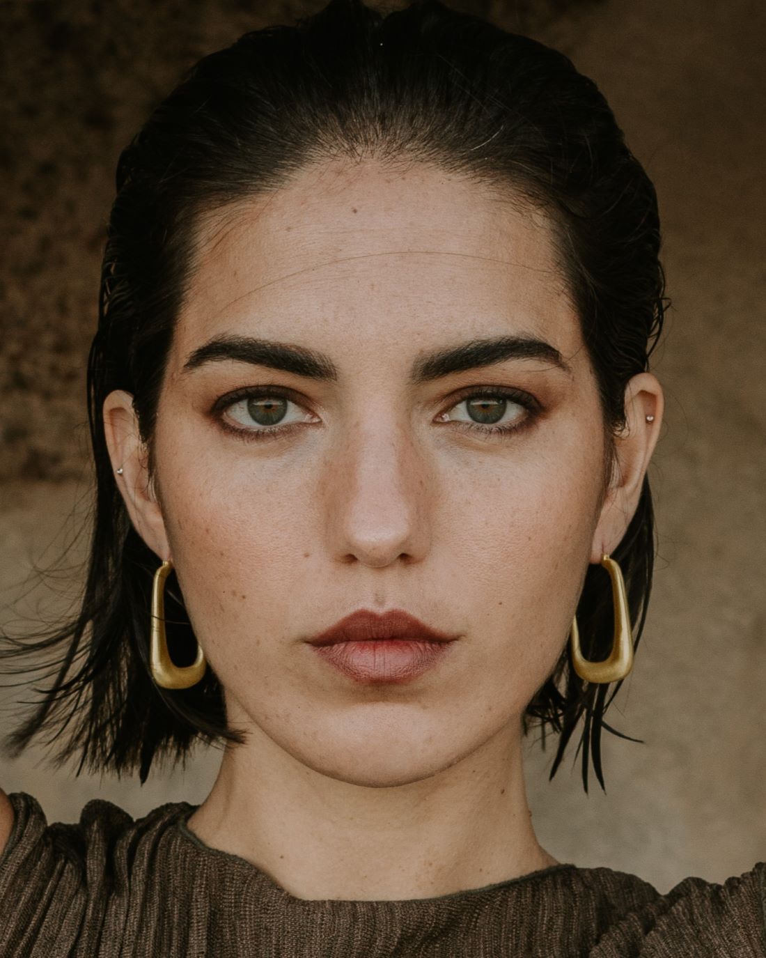 Modelo con pendientes dorados en forma de aro rectangular, diseño de Isla Vurma