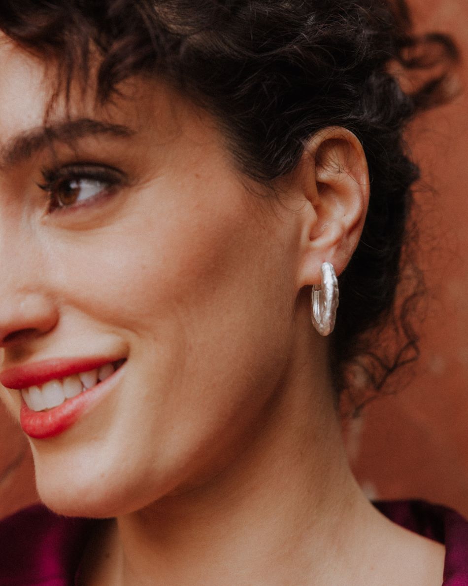 Primer plano de la modelo sonriente con los pendientes circulares irregulares bañados en plata de ley 925 de Isla Vurma