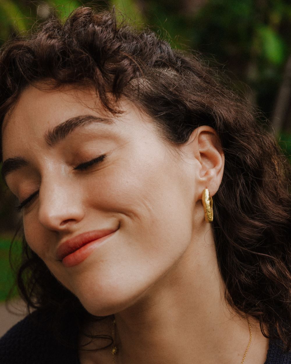 Primer plano de la modelo sonriente con los pendientes circulares irregulares bañados en oro de 18 quilates de Isla Vurma