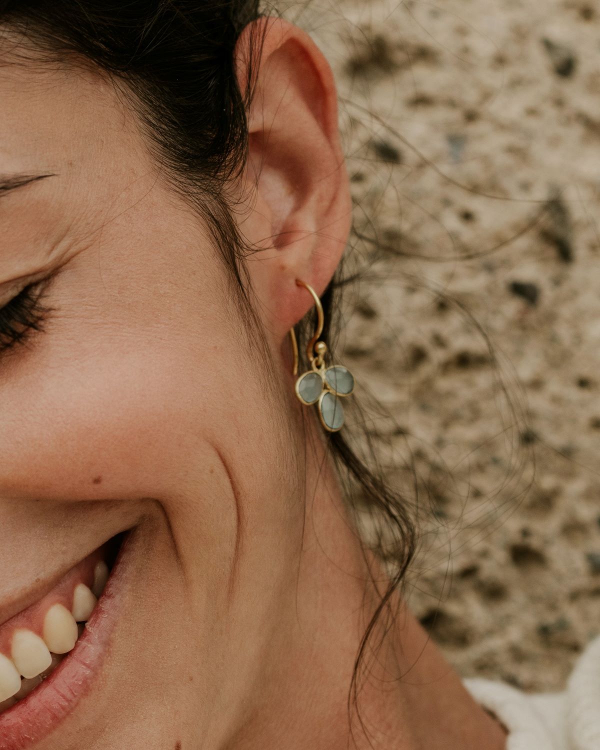 Modelo con pendientes elaborados con latón bañados en Oro de 18 quilates en forma de pétalo con piedra semipreciosa en Aqua Calcedonia incrustada y cierre de gancho abierto de Isla Vurma