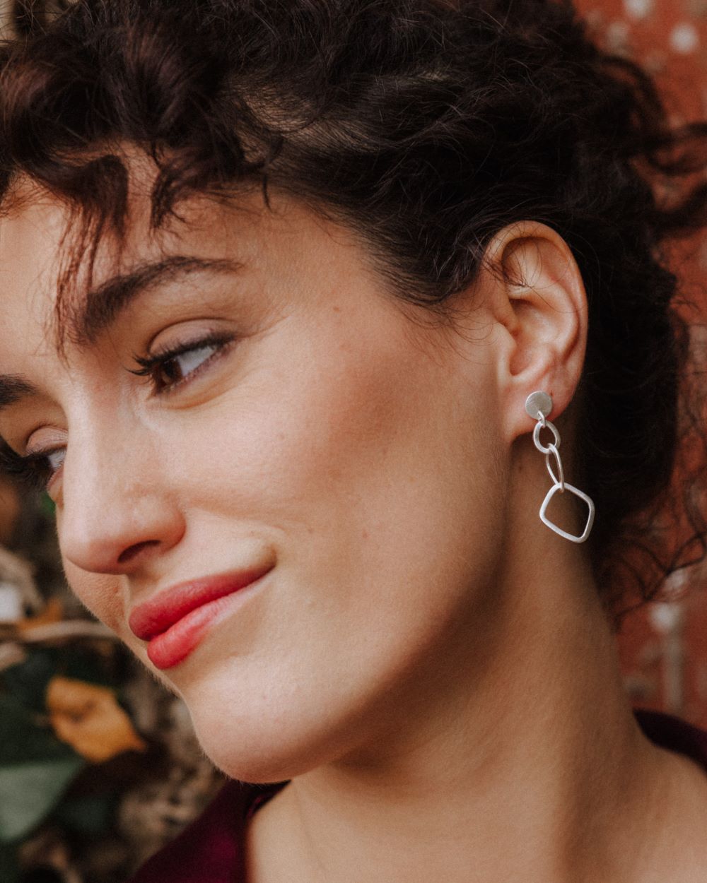 Primer plano de la modelo mirando hacia la izquierda sonriente con los pendientes geométricos largos bañados en plata de ley 925 de Isla Vurma