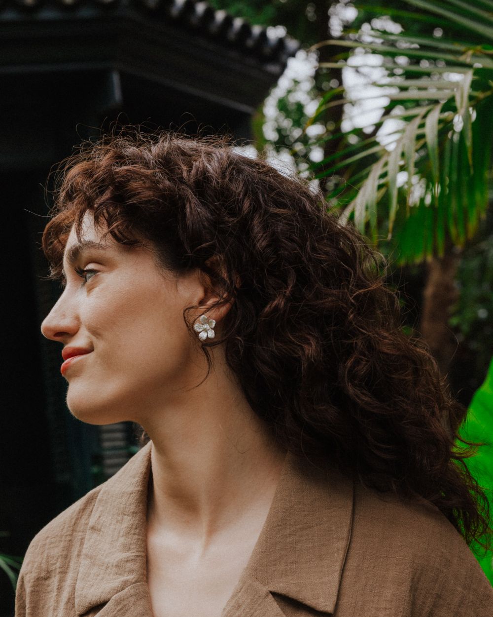 Pendientes plateados en forma de flor con textura detallada, lucidos por la modelo en un entorno natural.