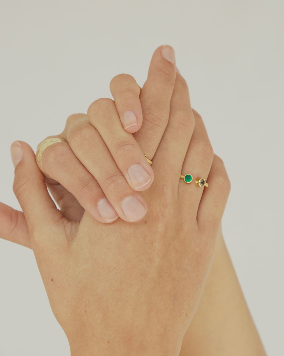 Primer plano de las manos de la modelo con el anillo de latón bañado en Oro de 18k de diseño abierto con dos pequeñas piedras semipreciosas en Amatista Verde y Ónix Verde en los extremos en forma redondeada