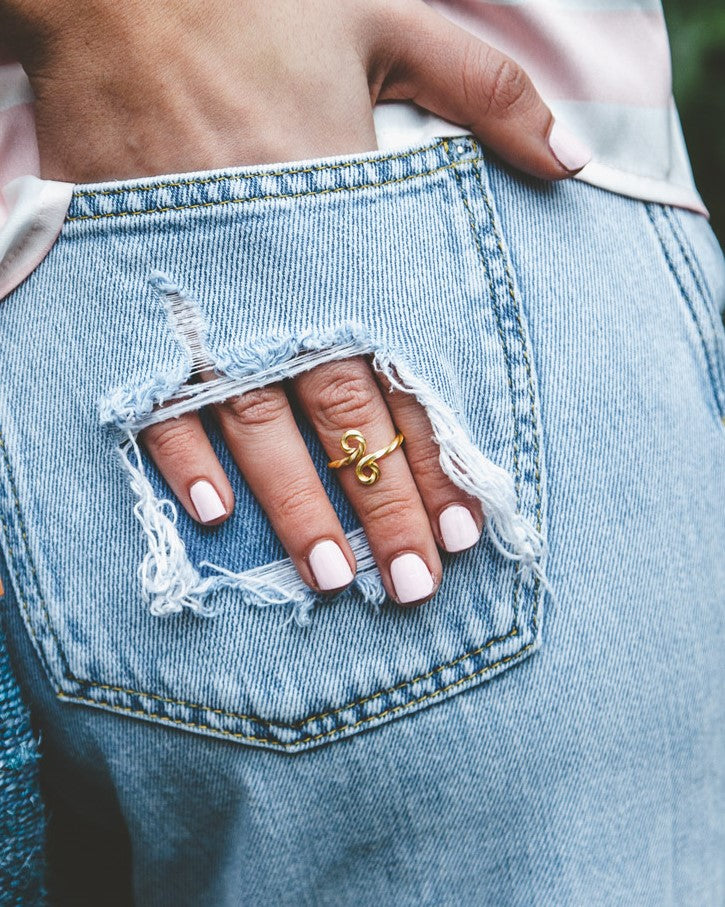 Primer plano de un bolsillo del pantalón vaquero de la modelo, con un agujero dónde se ve la mono con el anillo bañado en Oro de 18 quilates con un diseño trenzado y ondulado de Isla Vurma