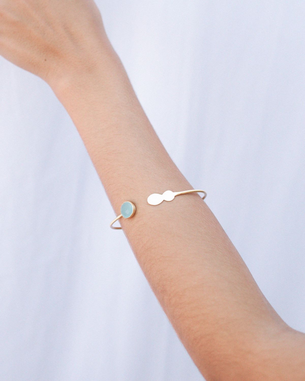 Primer plano del brazo de la modelo con el brazalete de latón bañado en oro de 18 quilates con una piedra semipreciosa en Aqua Calcedonia de Isla Vurma
