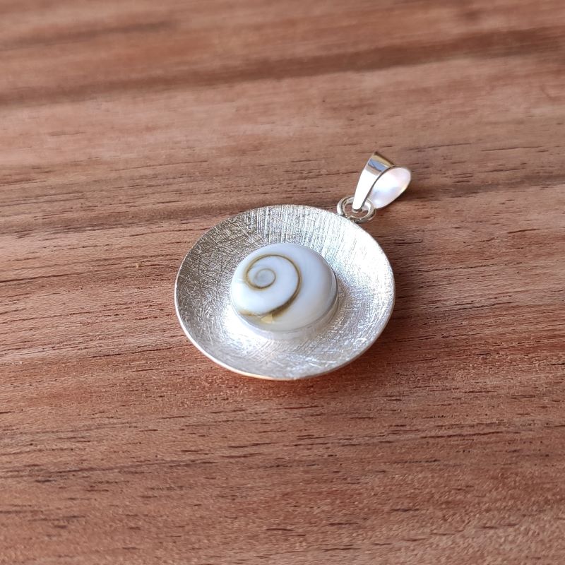 Primer plano del colgante que presenta una piedra de Santa Lucía enmarcada en un disco de textura cepillada