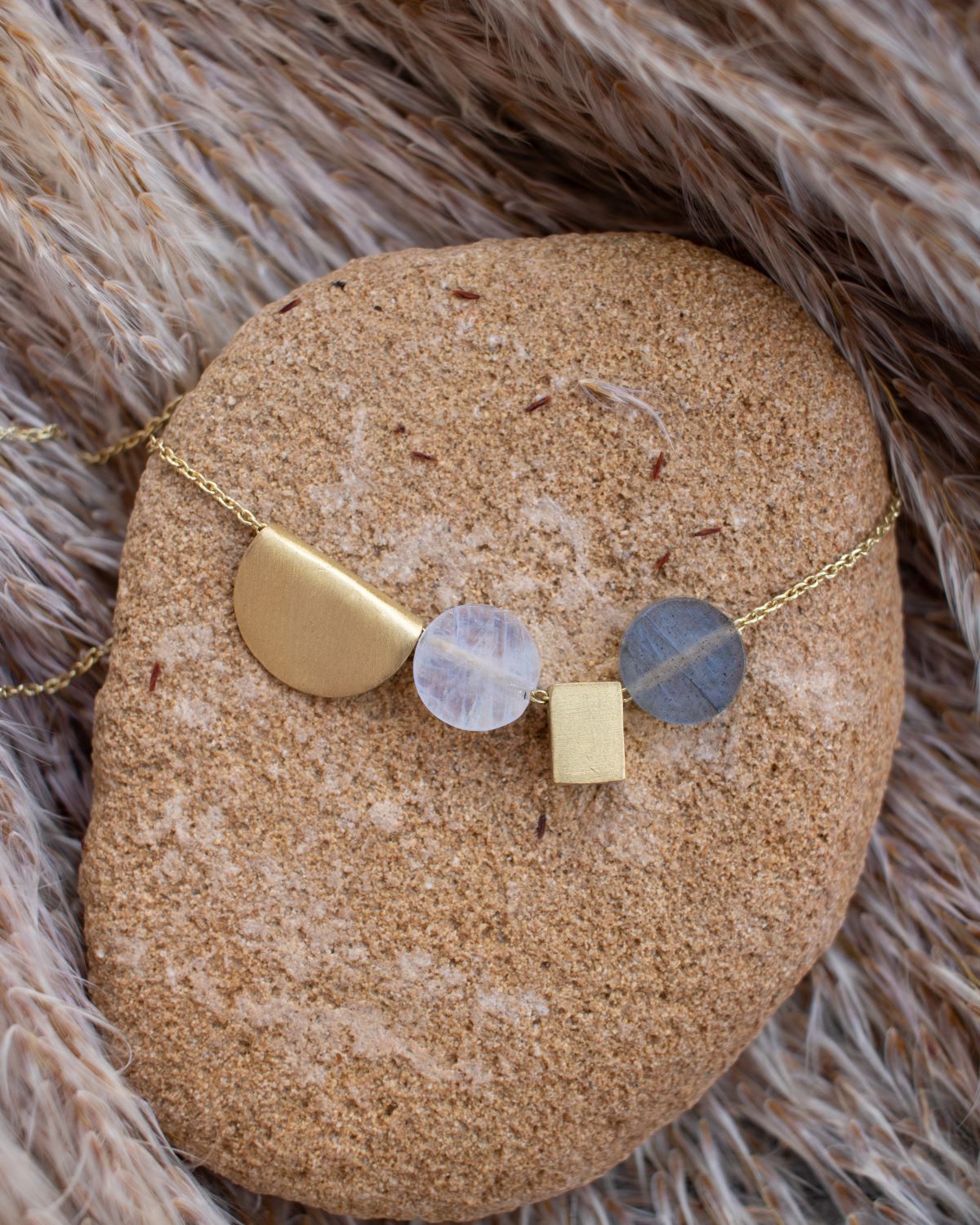 Primer plano de collar apoyado en piedra natural, collar compuesto por figuras geométricas bañadas en oro y piedras semipreciosas Moonstone y Labradorita de Isla Vurma