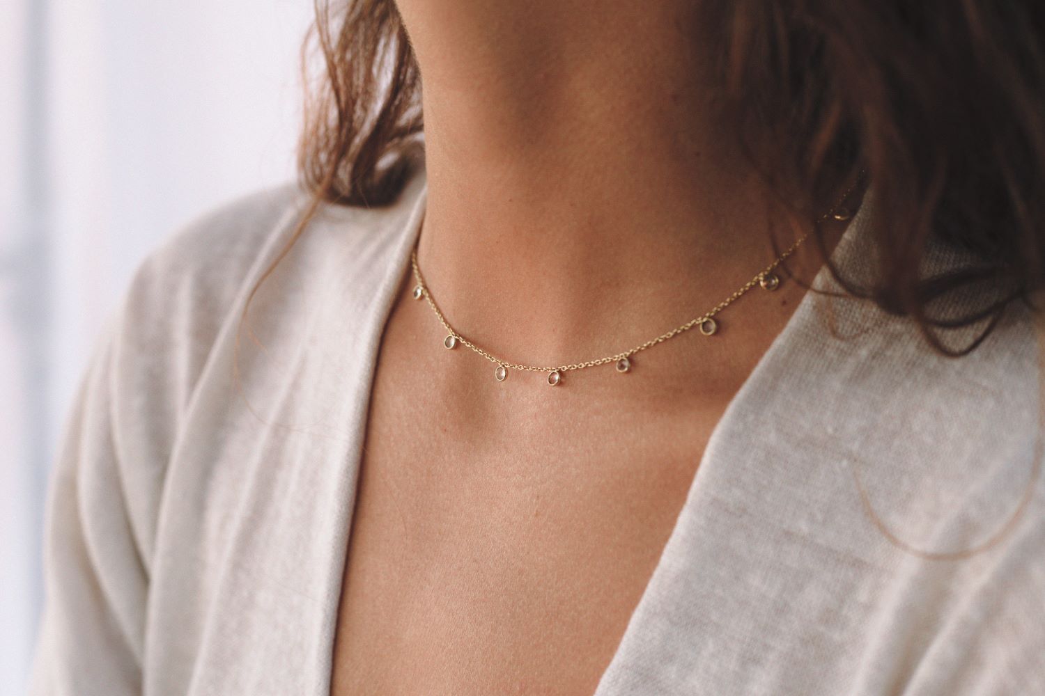 Mujer con cabello suelto lleva un collar dorado con pequeños colgantes circulares con piedras semipreciosas de Cuarzo Rosa de Isla Vurma