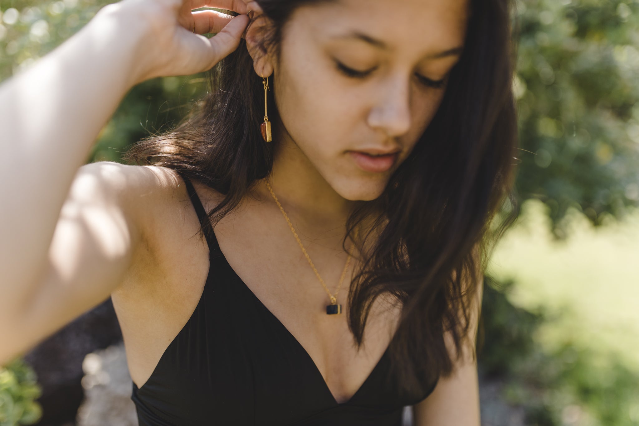 Mujer con vestido negro lleva un collar dorado con colgante de Lapislázuli y pendientes largos con forma triangular dorada de Isla Vurma
