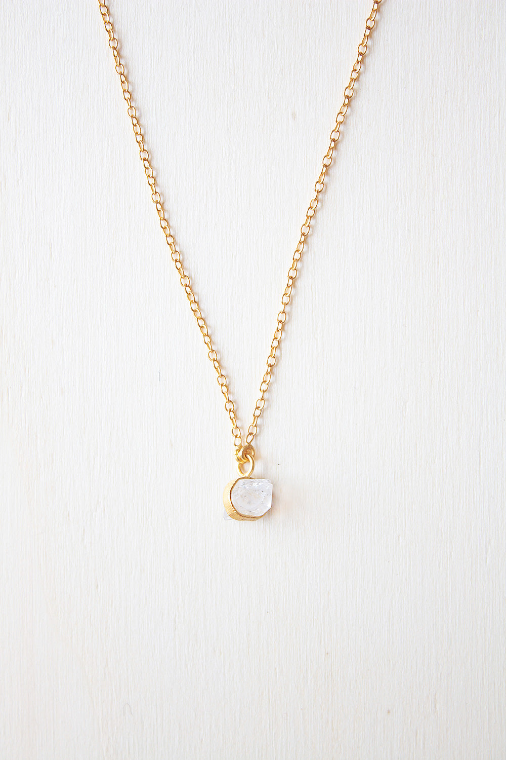 Collar bañado en oro de 18 quilates, con piedra semipreciosa Piedra de Luna, sujetada por una pequeña pieza rectangular dorada en un fondo blanco de Isla Vurma