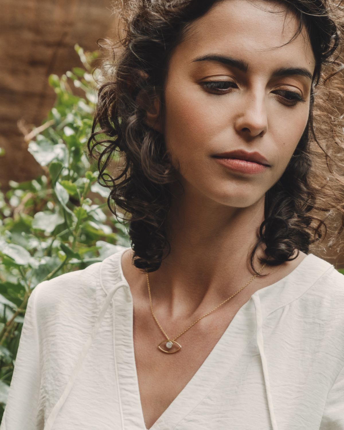 Primer plano de la modelo con una camiseta blanca y el collar bañado en oro de 18 quilates con un colgante en forma de ojo y piedra semipreciosa en Piedra de Luna de Isla Vurma
