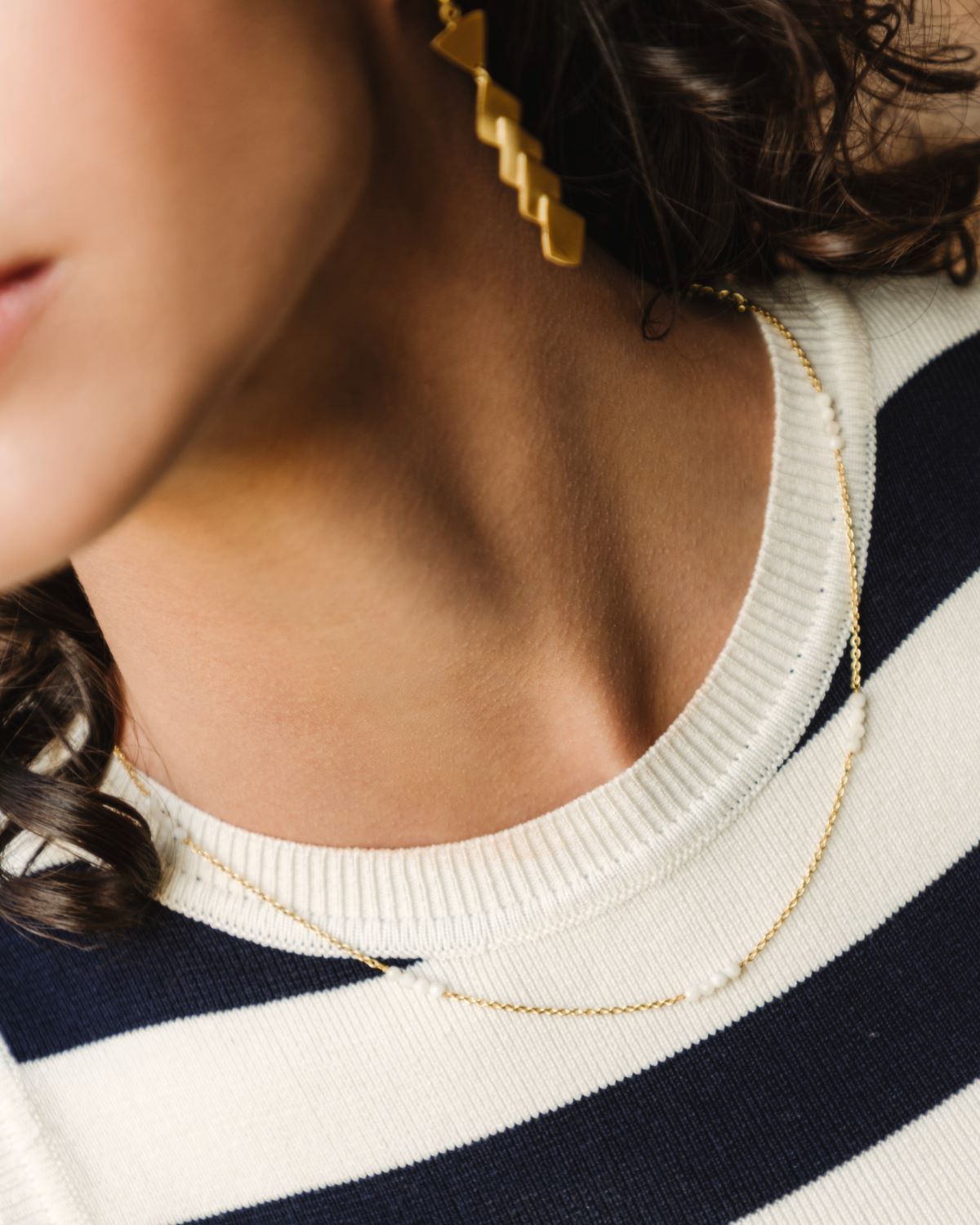 Modelo con pendientes dorados y collar bañado en oro de 18 quilates compuesto por pequeñas tiras de piedras semipreciosas Piedra de Luna de Isla Vurma