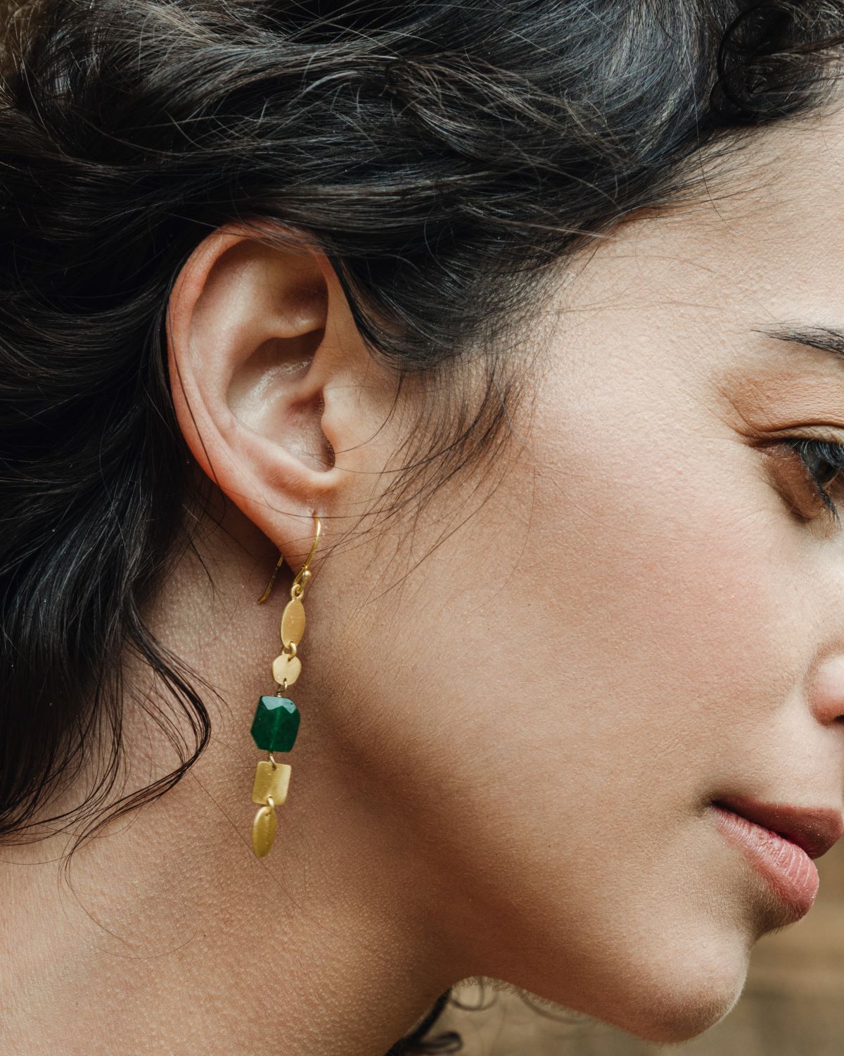 Pendiente largo con baño de oro, formado por piezas geométricas de acabado mate y una piedra semipreciosa Jade facetada en el centro lucido por la modelo