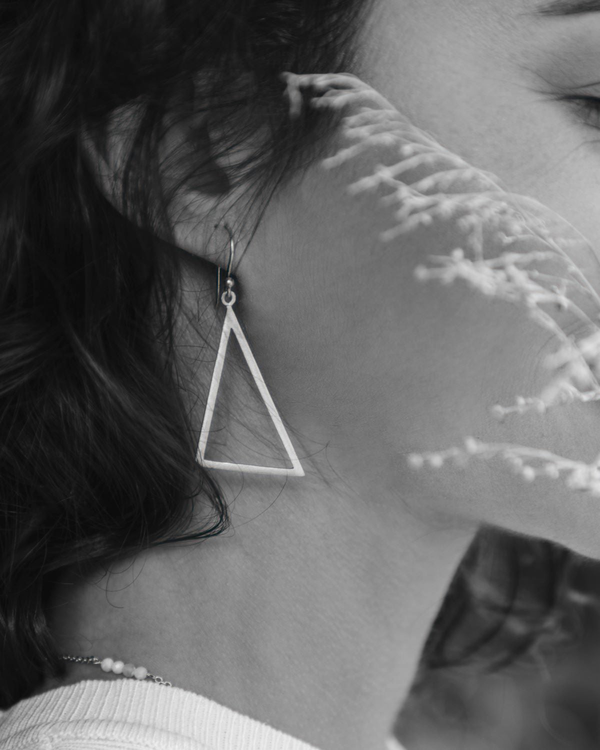Pendiente triangular grande en acabado plata 925 sobre la oreja, con un efecto artístico en blanco y negro.