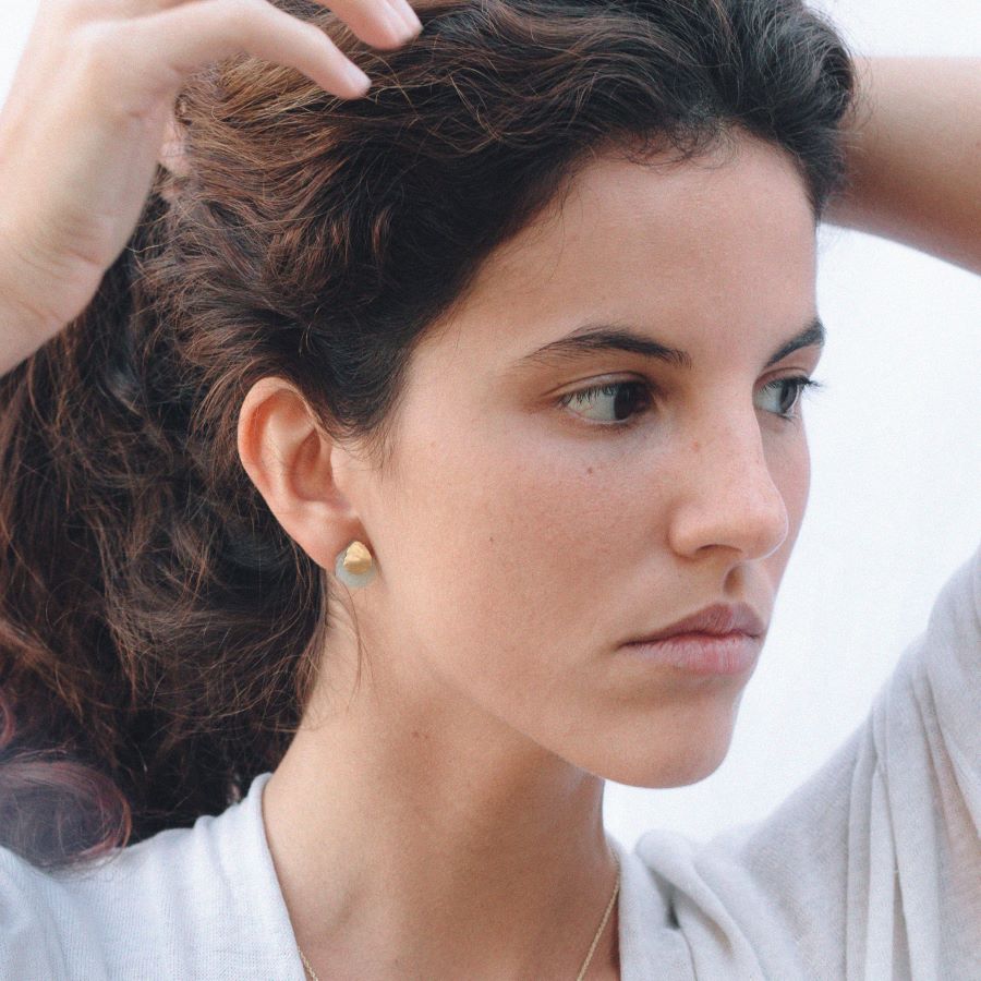 Pendientes con base dorada de forma orgánica y piedra semipreciosa Aqua calcedonia, ajustados al lóbulo de la oreja de la modelo.
