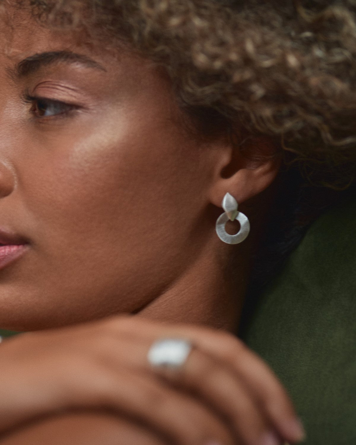 Primer plano de la modelo con pendientes bañados en plata 925 de diseño circular y hoja superior, acabado satinado, fondo difuminado