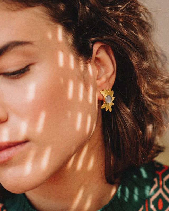 pendientes dorados con diseño de hojas y piedra central en Piedra Luna en la oreja de la modelo bajo luz natural