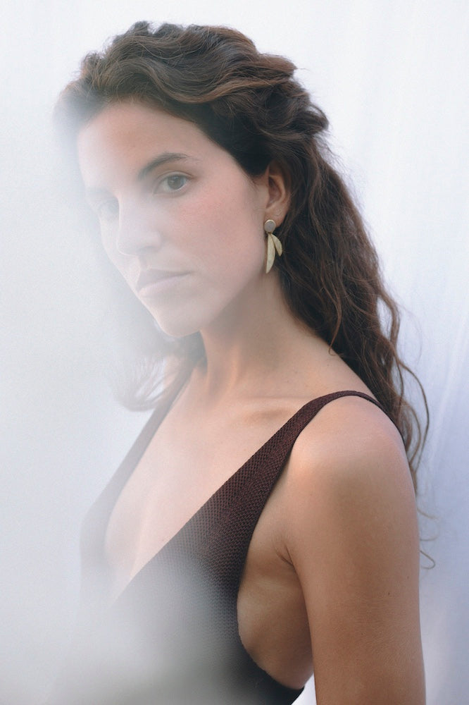 Pendientes dorados con diseño de hojas y Piedra de Luna combinados con un vestido de tirantes, mostrados en un retrato vertical con efecto bruma en primer plano.