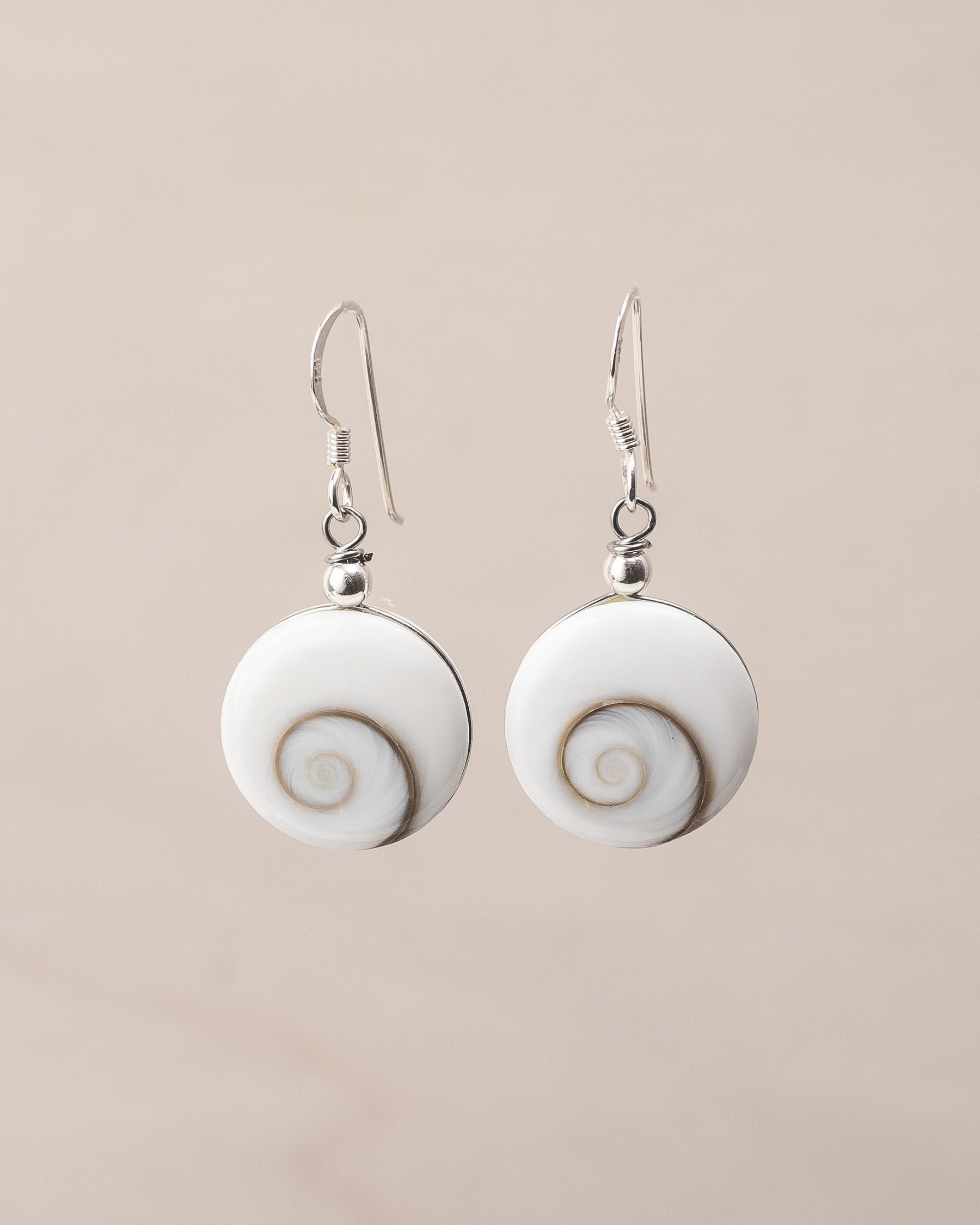 Pendientes artesanales de plata de ley con Ojo de Santa Lucía. Concha formada por espiral natural y montura de plata de ley sobre fondo neutro