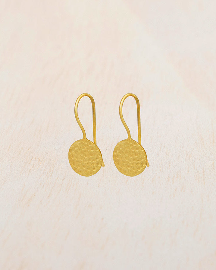 Pendientes circulares de latón bañados en oro de 18 quilates con textura martillada sobre fondo beige claro