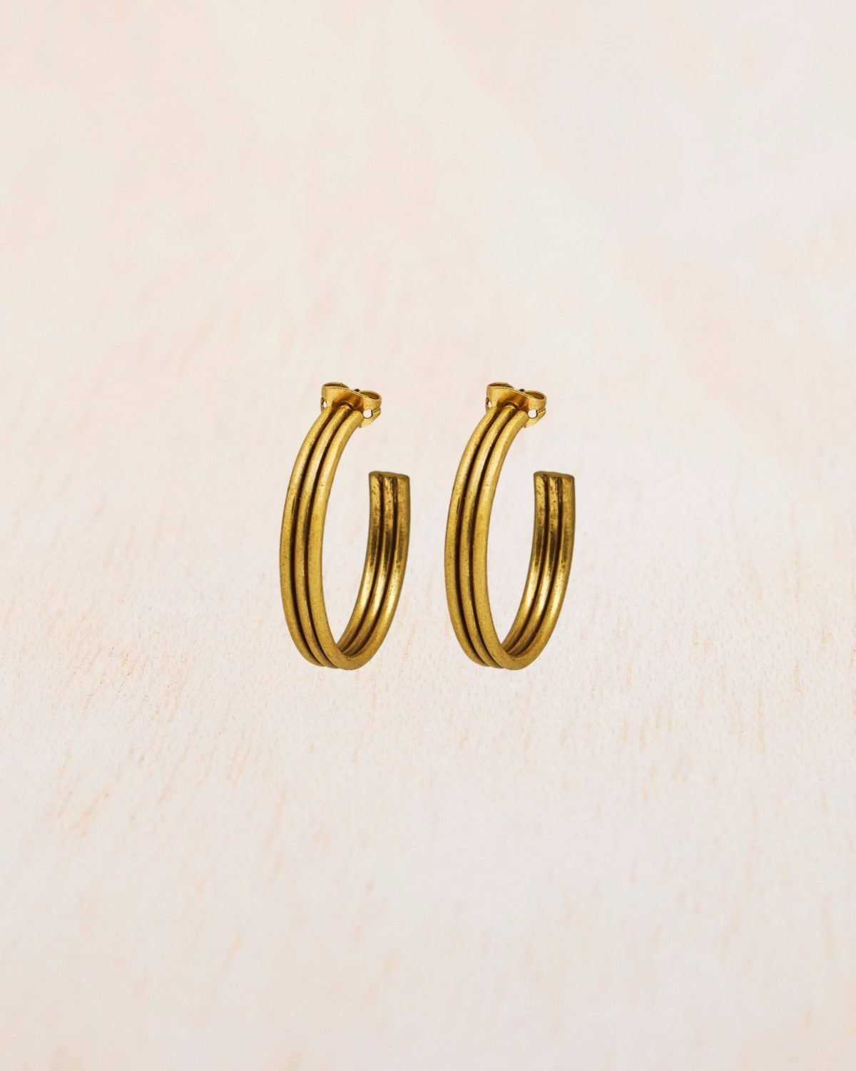 Aros dorados gruesos de acabado pulido sobre fondo beige claro