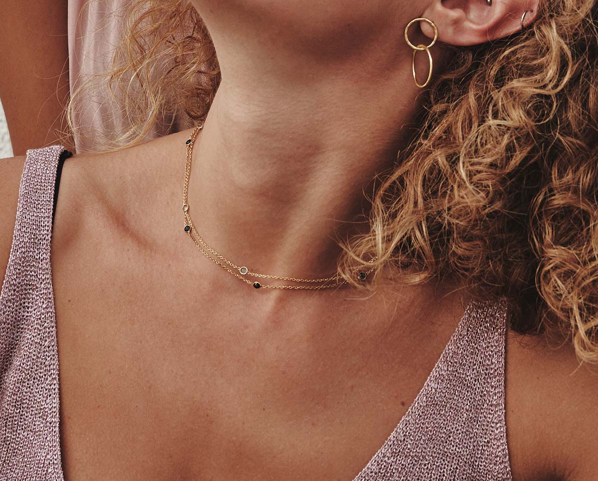 Primer plano de collares dorados con piedra semipreciosa Aventurina Verde y Multicolor, además de unos pendientes circulares dorados de Isla Vurma