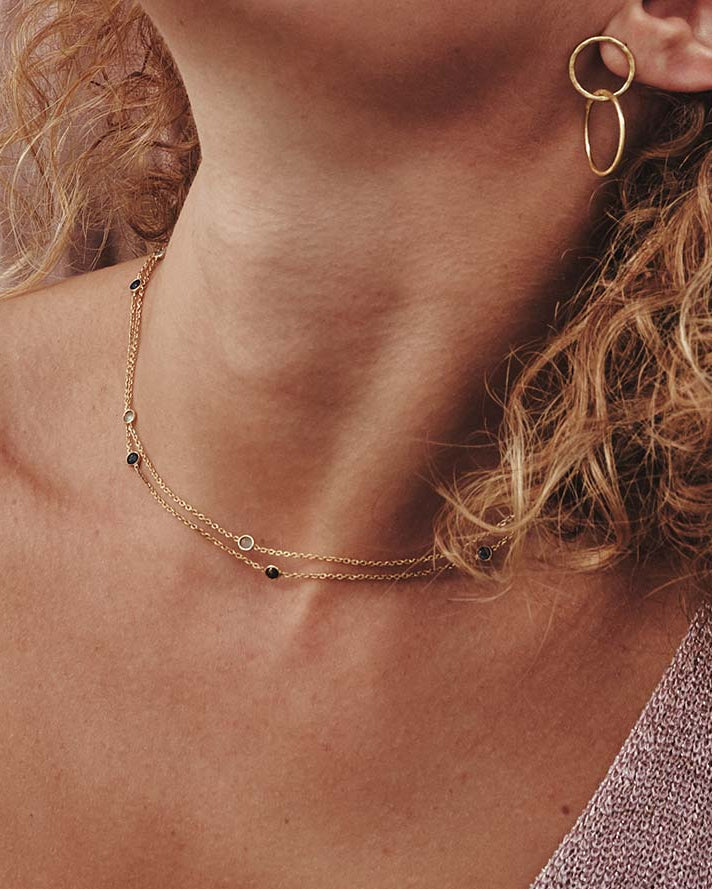 Primer plano de collares dorados con piedra semipreciosa Aventurina Verde y Multicolor, además de unos pendientes circulares dorados de Isla Vurma