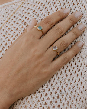 Mano de la modelo con el anillo bañado en oro con piedra central cuadrada en Aqua Calcedonia y Cuarzo Rosa