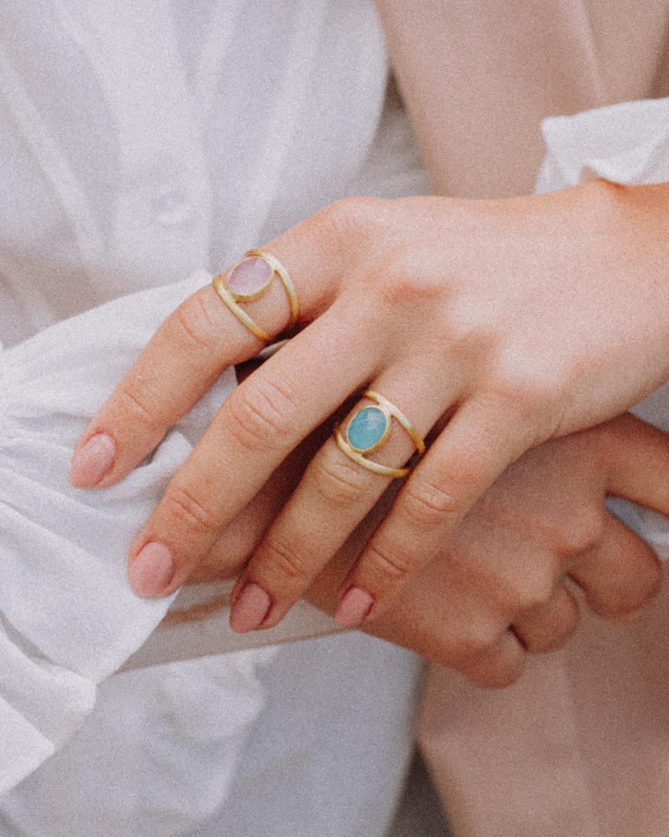 Primer plano de la mano de la modelo con conjunto de anillos bañados en Oro de 18k con piedra semipreciosa Aqua Calcedonia y Cuarzo Rosa talladas en forma ovalada