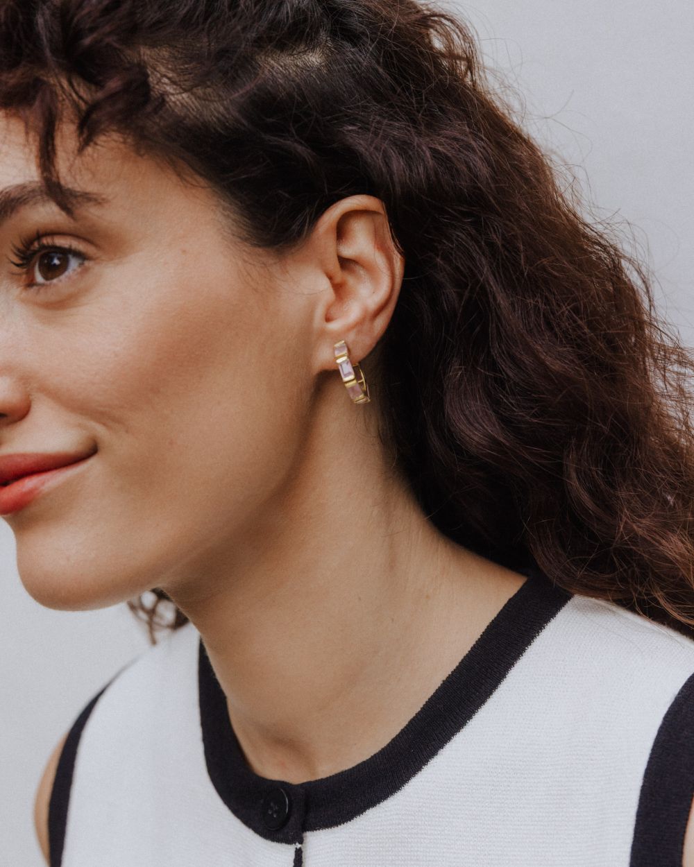 Pendiente de aro dorado con piedras rectangulares semipreciosas en Cuarzo Rosa, lucido en la oreja de la modelo de cabello oscuro y suelto. 