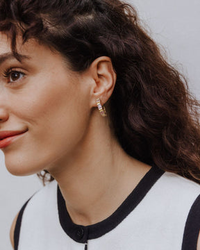 Pendiente de aro dorado con piedras rectangulares semipreciosas en Cuarzo Rosa, lucido en la oreja de la modelo de cabello oscuro y suelto. 