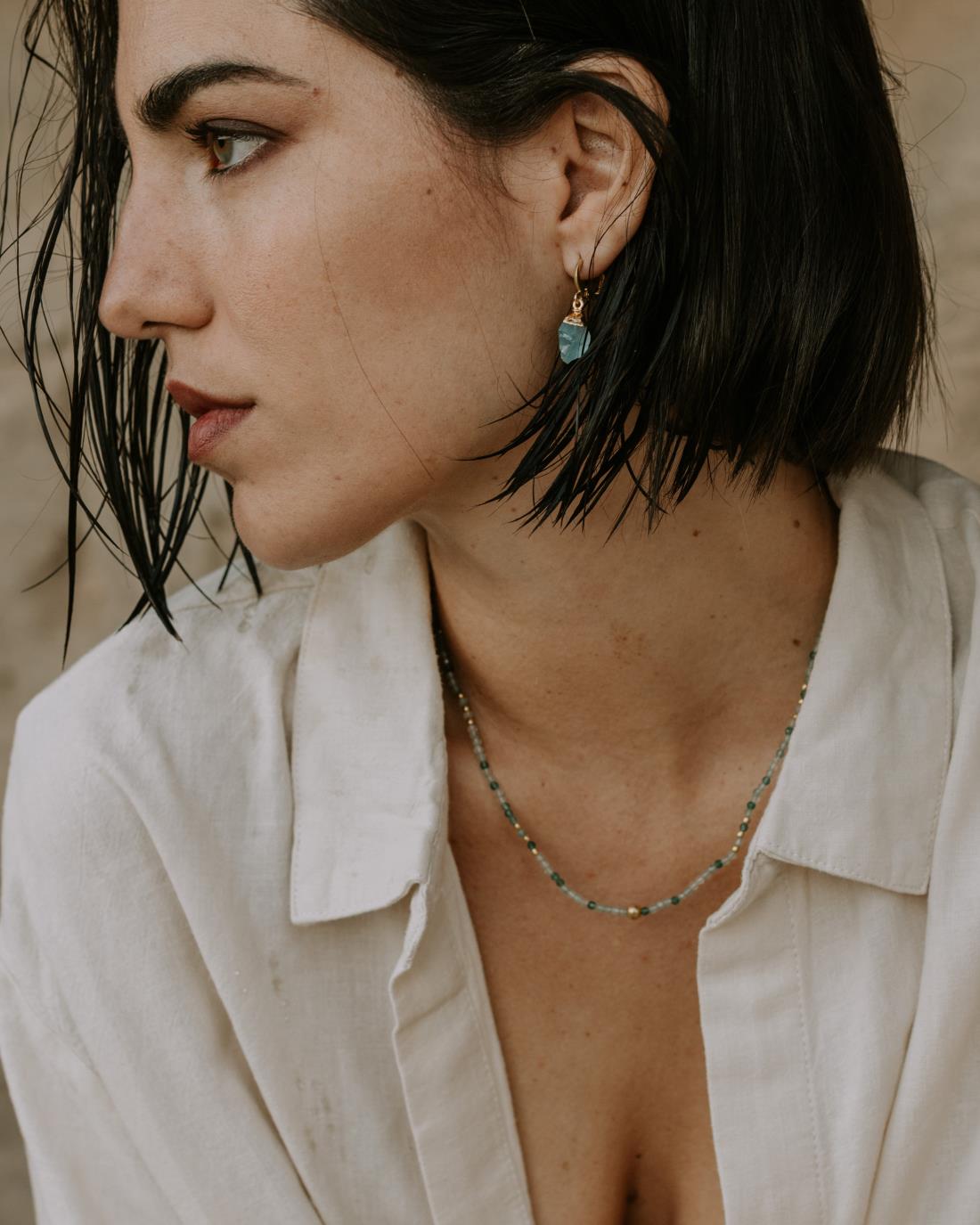 Modelo con collar en tonos verdosos y pendientes de color turquesa y oro