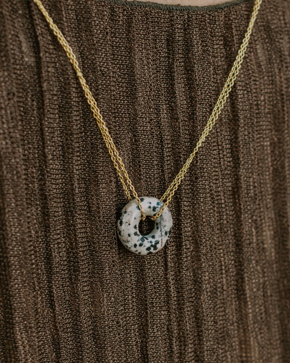 Primer plano del collar Ofelia, elaborado con un Jaspe Dálmata circular con abertura interior y cadena de latón bañada en Oro de 18 quilates