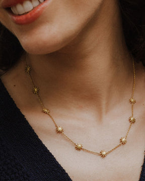 Primer plano de la modelo sonriendo que lleva un collar dorado con pequeños colgantes en forma de estrella de ocho puntas