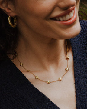 Primer plano de la modelo sonriendo que lleva un collar dorado con pequeñas estrellas distribuidas a lo largo de la cadena y unos aros dorados texturizados