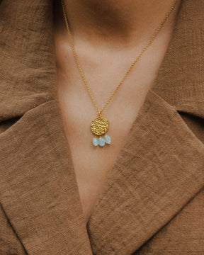 Primer plano del cuello de la modelo llevando el collar bañado en oro de 18 quilates con una pieza circular martillado con tres piedras semipreciosas en forma de gota en Aqua Calcedonia de Isla Vurma
