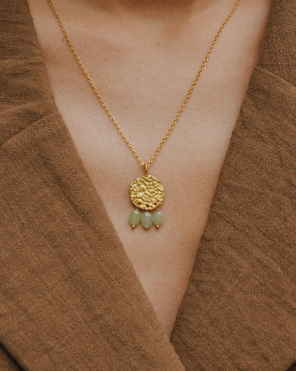 Primer plano del cuello de la modelo llevando el collar bañado en oro de 18 quilates con una pieza circular martillado con tres piedras semipreciosas en forma de gota en Aventurina Verde de Isla Vurma