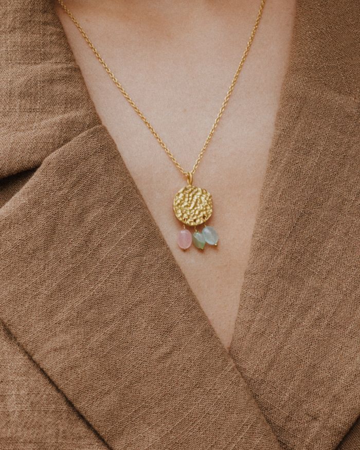 Primer plano del cuello de la modelo llevando el collar bañado en oro de 18 quilates con una pieza circular martillado con tres piedras semipreciosas en forma de gota en Aventurina Verde, Aqua Calcedonia y Cuarzo Melocotón de Isla Vurma