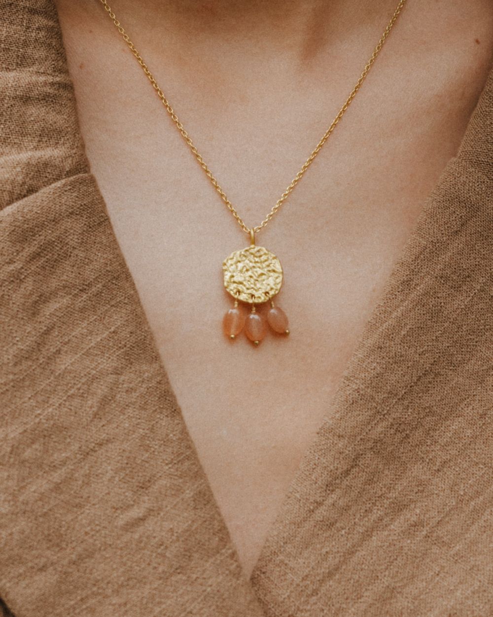 Primer plano del cuello de la modelo llevando el collar bañado en oro de 18 quilates con una pieza circular martillado con tres piedras semipreciosas en forma de gota en Cuarzo Melocotón de Isla Vurma