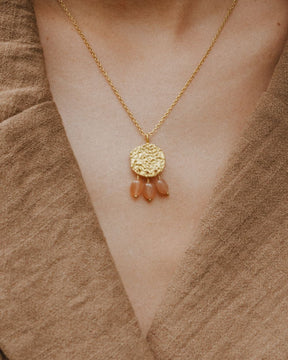 Primer plano del cuello de la modelo llevando el collar bañado en oro de 18 quilates con una pieza circular martillado con tres piedras semipreciosas en forma de gota en Cuarzo Melocotón de Isla Vurma