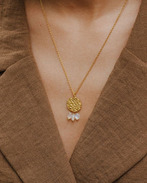 Primer plano del cuello de la modelo llevando el collar bañado en oro de 18 quilates con una pieza circular martillado con tres piedras semipreciosas en forma de gota en Piedra de Luna de Isla Vurma